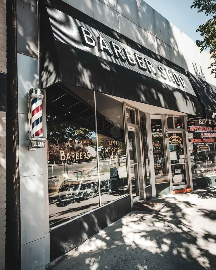 The City Barbers storefront with its awning and barber pole on a sunny day