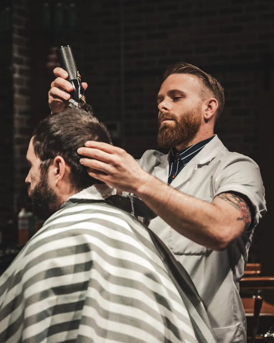 A bearded barber combing through a client’s hair
