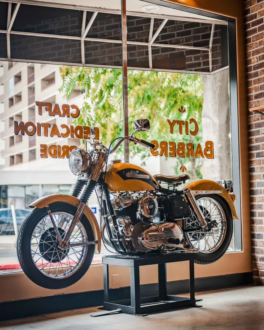 A vintage motorcycle in the City Barbers front window during the day