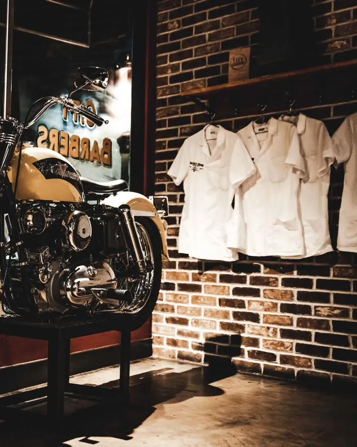 City Barbers shirts hanging on the brick wall beside a vintage motorcycle