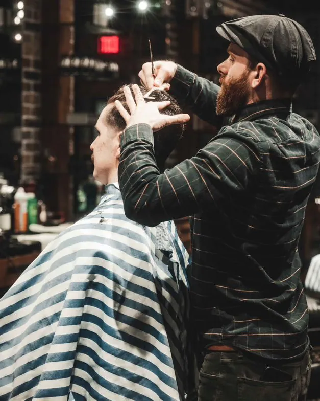 A barber in a flat cap cutting hair with scissors