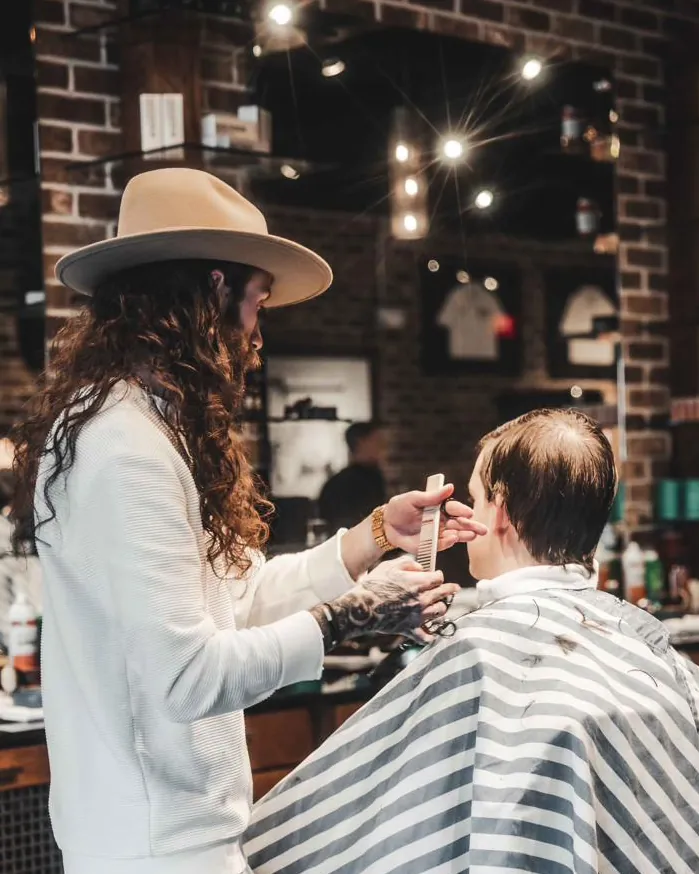 A barber in a wide-brimmed hat cutting a client’s hair