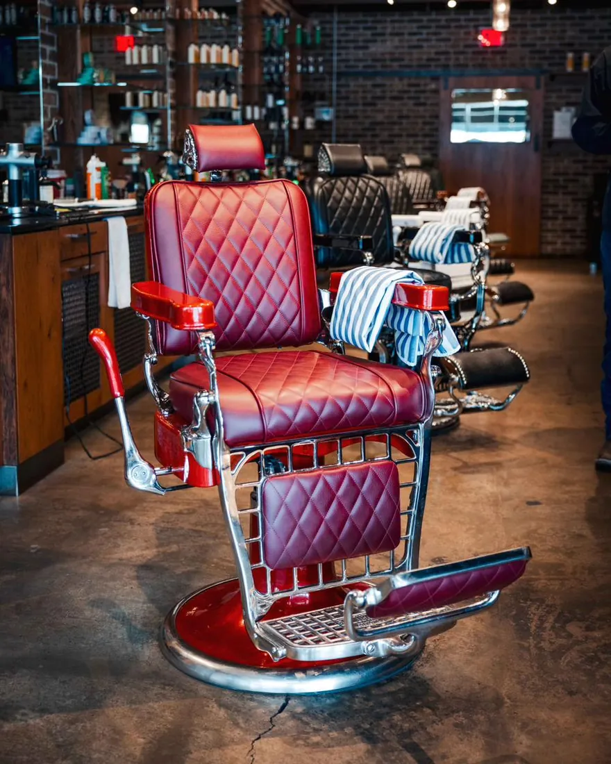 A red leather barber chair at the front of a row of chairs