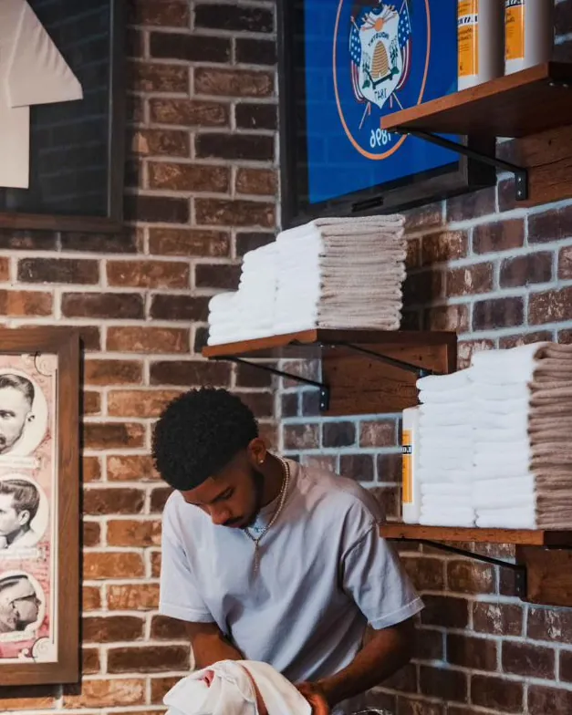 A barber at the wash basin beneath vintage haircut posters