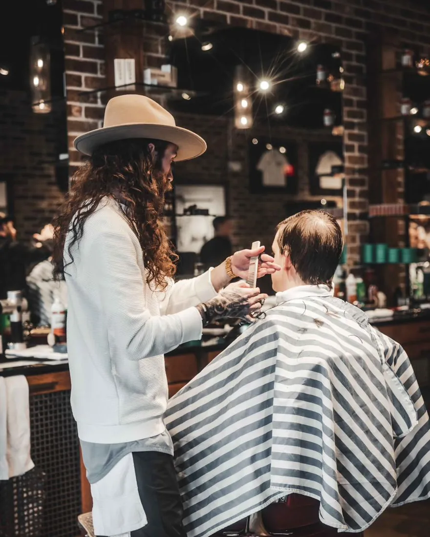 A barber in a wide-brimmed hat working on a client’s haircut
