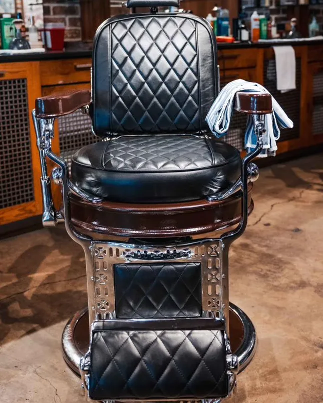 A black leather barber chair with a towel over the arm