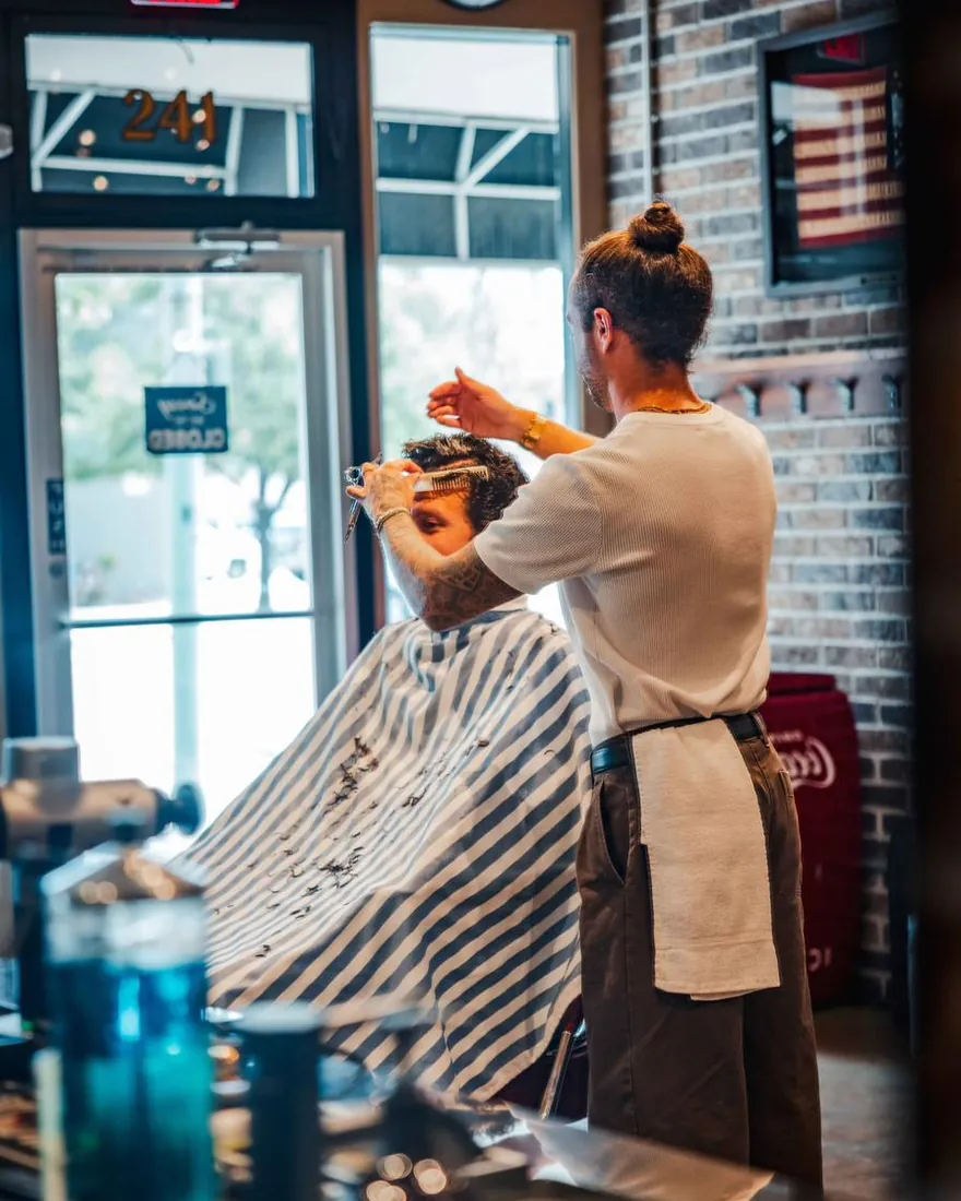 A barber cutting a client’s hair beside the shop’s front window