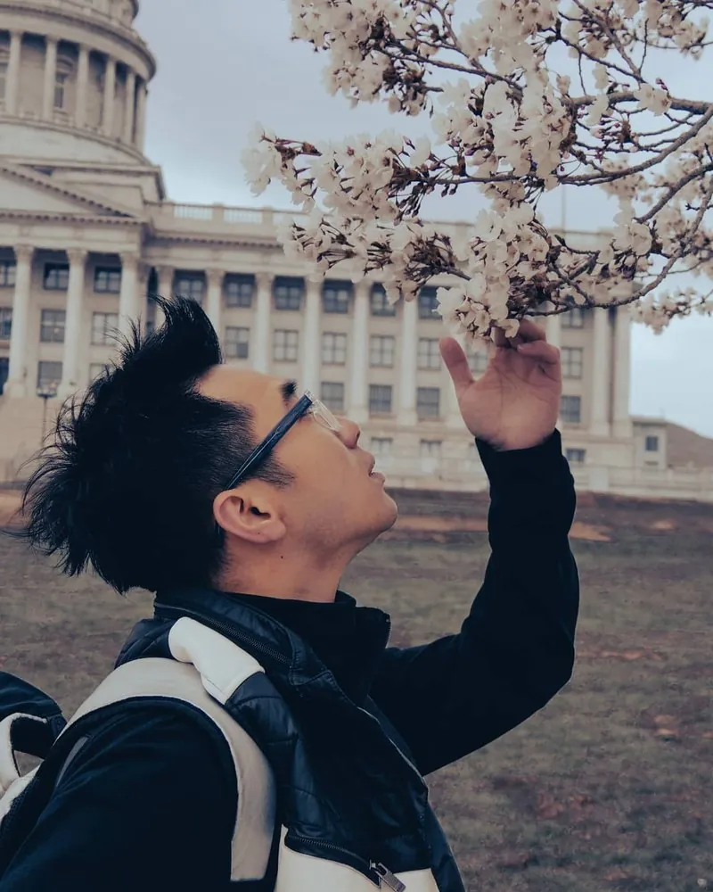 Bao Wow, a barber at City Barbers, outdoors under spring blossoms