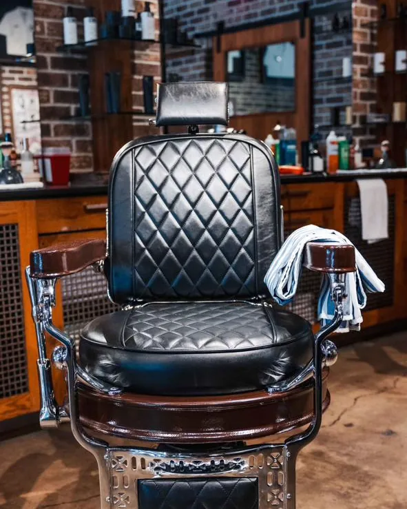 A black leather barber chair with a towel over the arm