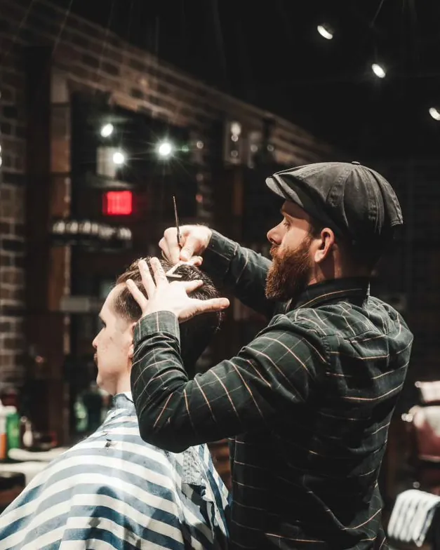 A barber in a flat cap with scissors, mid-cut