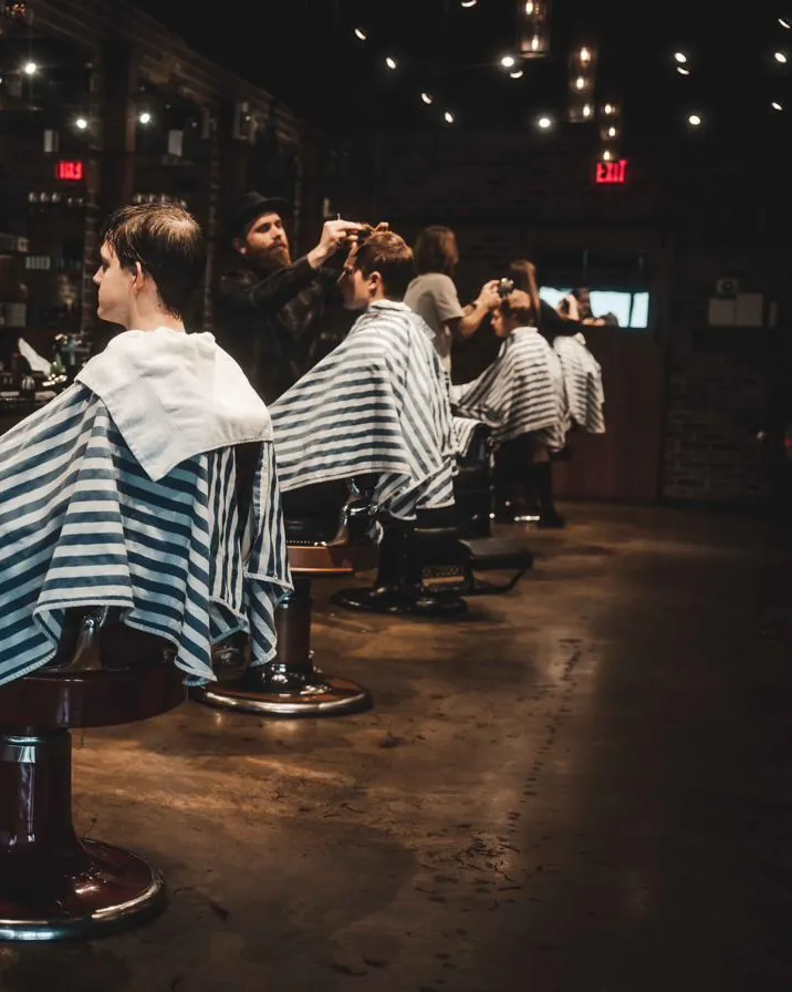 Clients in striped capes along the row of barber chairs