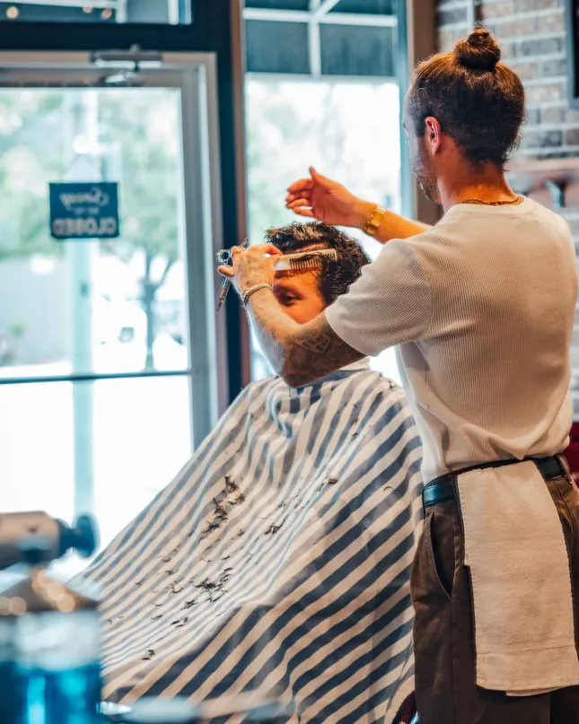 A barber cutting a client’s hair by the front window
