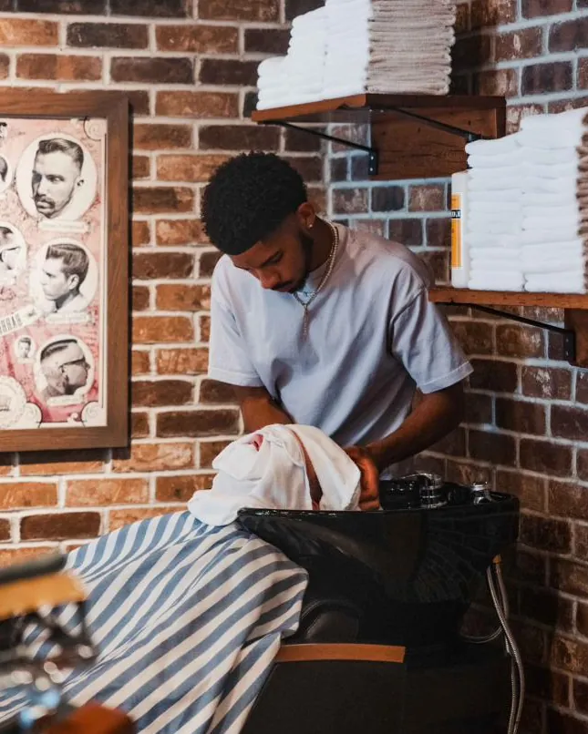 A barber rinsing a client’s hair at the basin